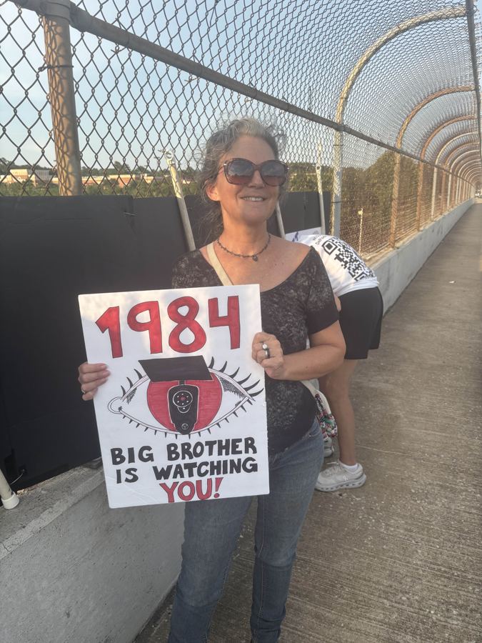 Volunteer holding a 1984 Big Brother is watching you sign on the bridge